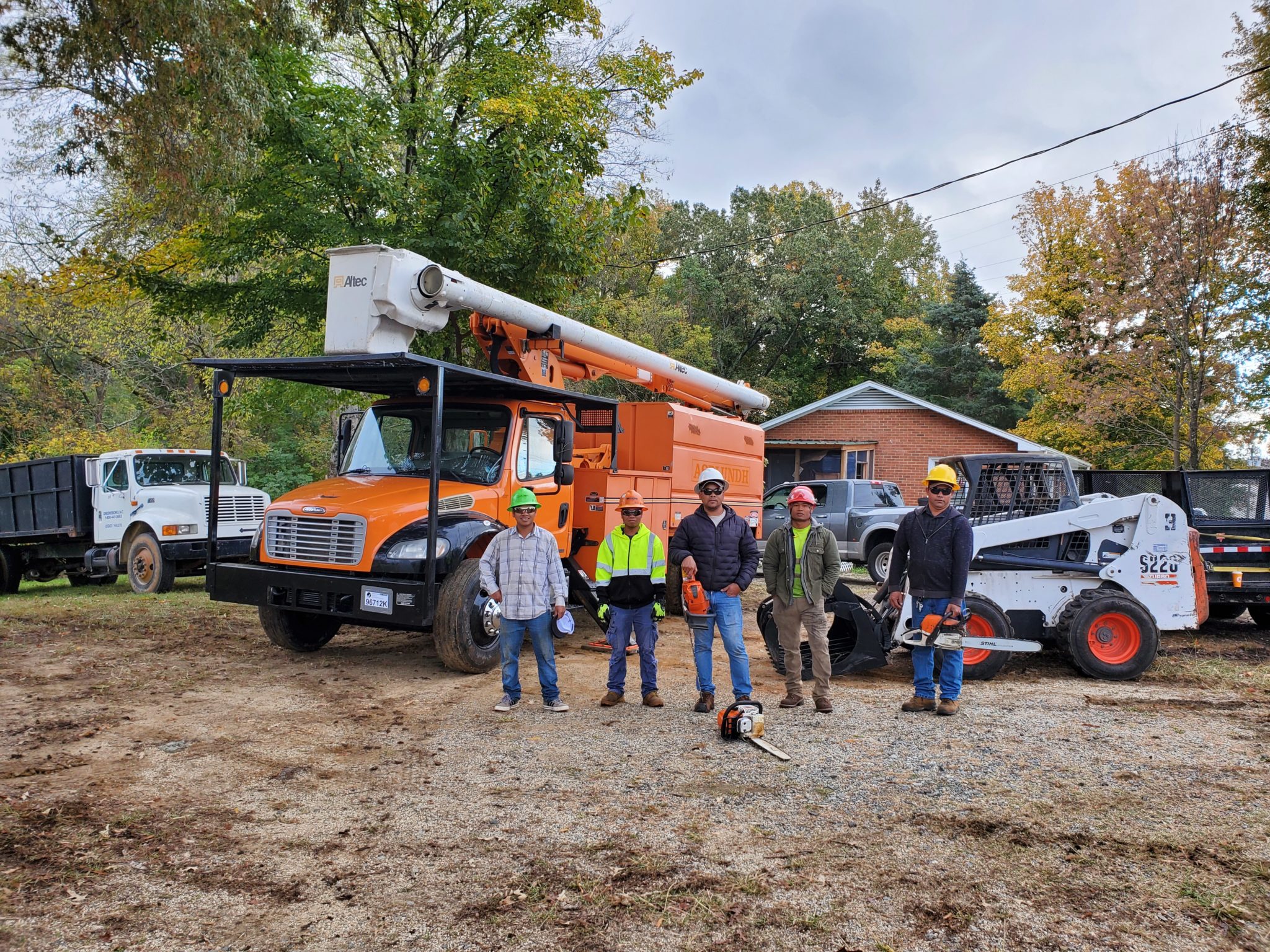 The image shows a group of six people standing in front of an orange Altec bucket truck